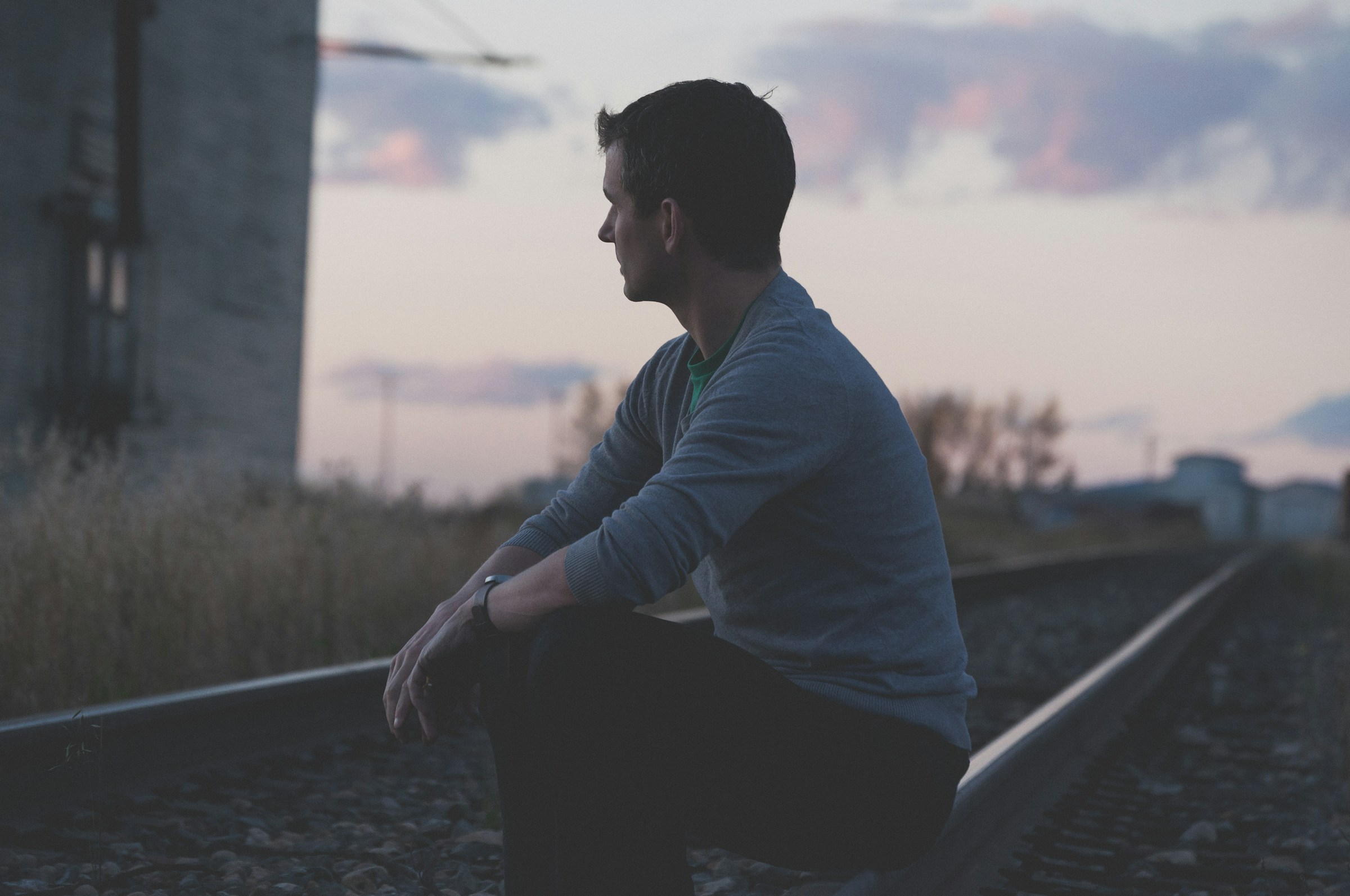A man sits pensively on railroad tracks as dusk falls around him.