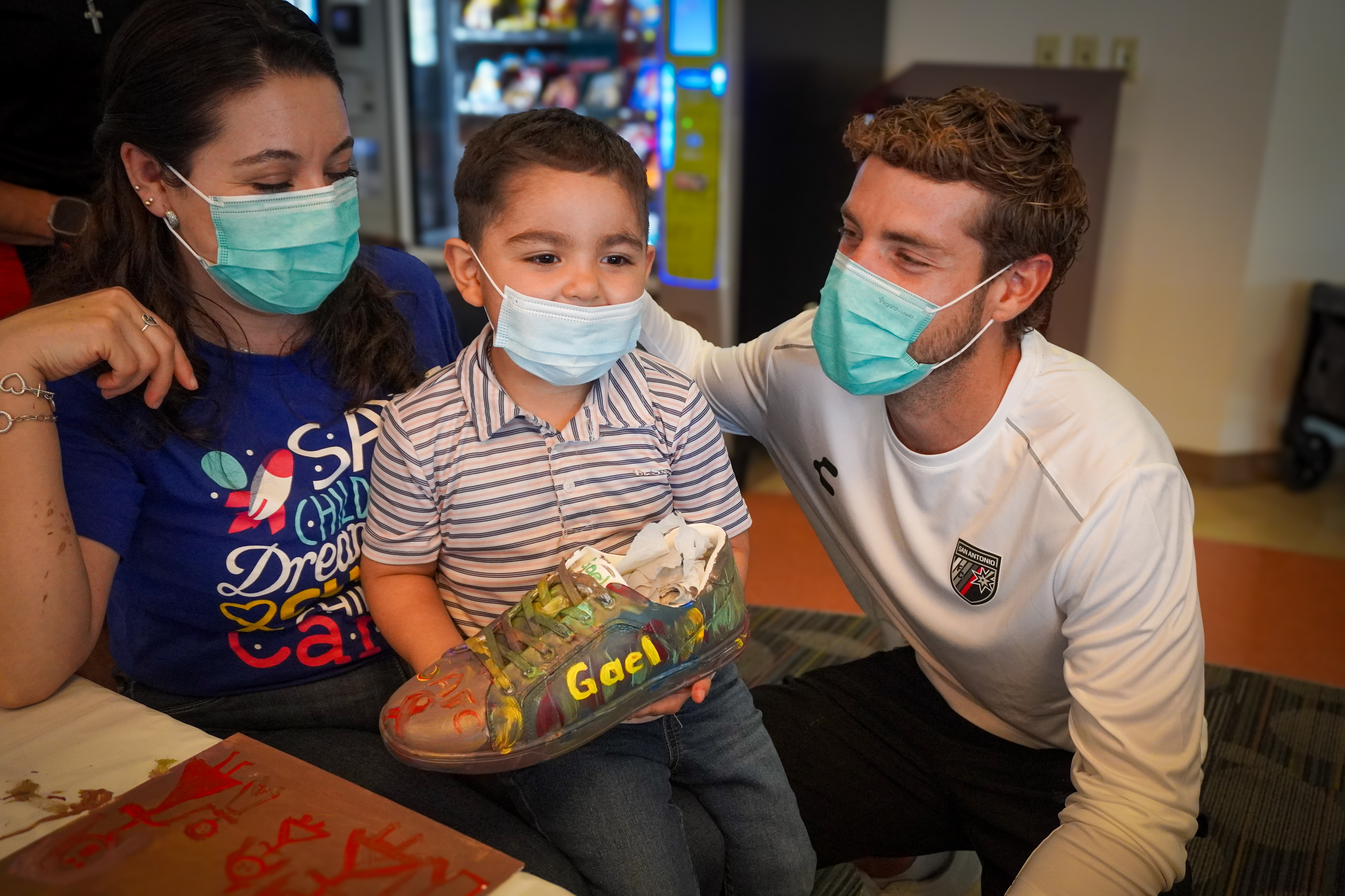 San Antonio FC Player poses with pediatric oncology patient and custom-designed shoe at Methodist Children's Hospital.