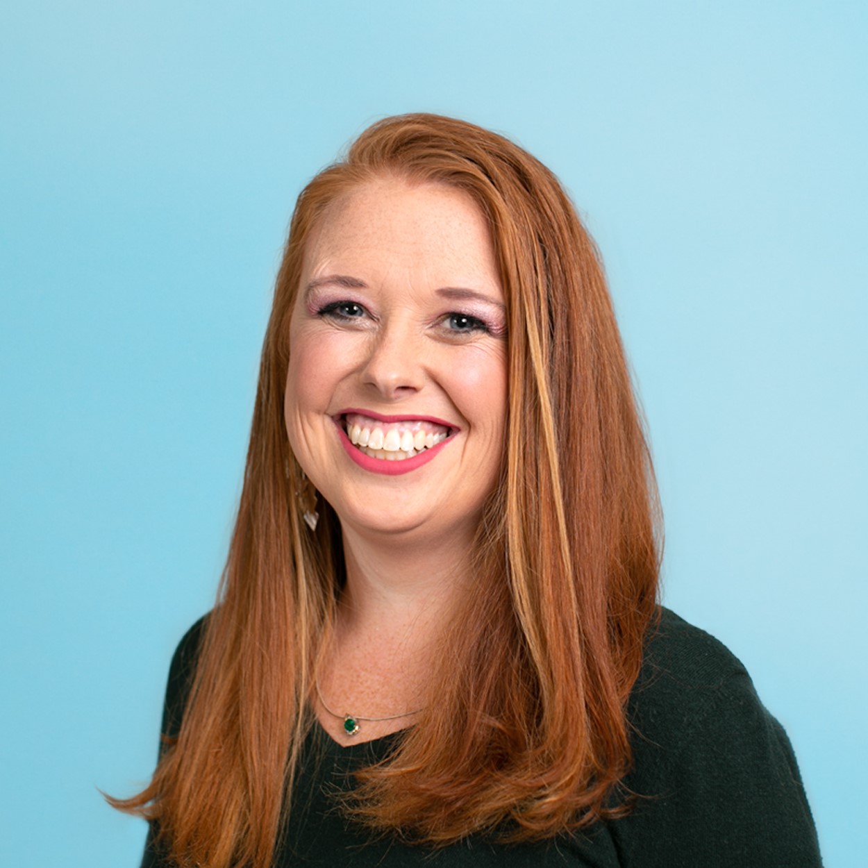 Nora smiles for the camera, while seated in a chair and wearing a black sweater.