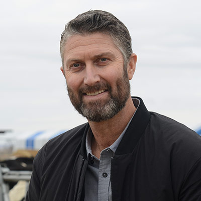 William DeJong stands outside on his dairy farm, in front of a row of cattle.