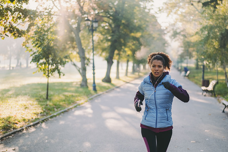 A woman jogs in the park in winter while she wears gloves and a puffy jacket.