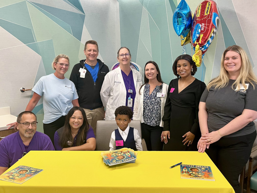 Male and female hospital staff surround young boy Payton seated at a table with books. 