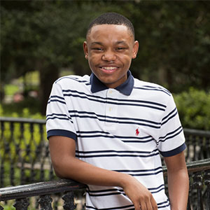 Tre Jenkins smiles while wearing a black and white stripe shirt and leaning on a fence rail.