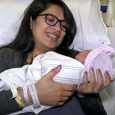 Niyati Desai smiling and holding her newborn from a patient bed.