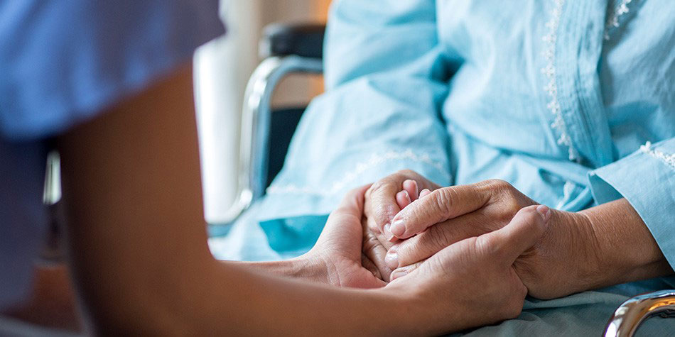 A nurse holds a patients hands who is sitting in a wheelchair.