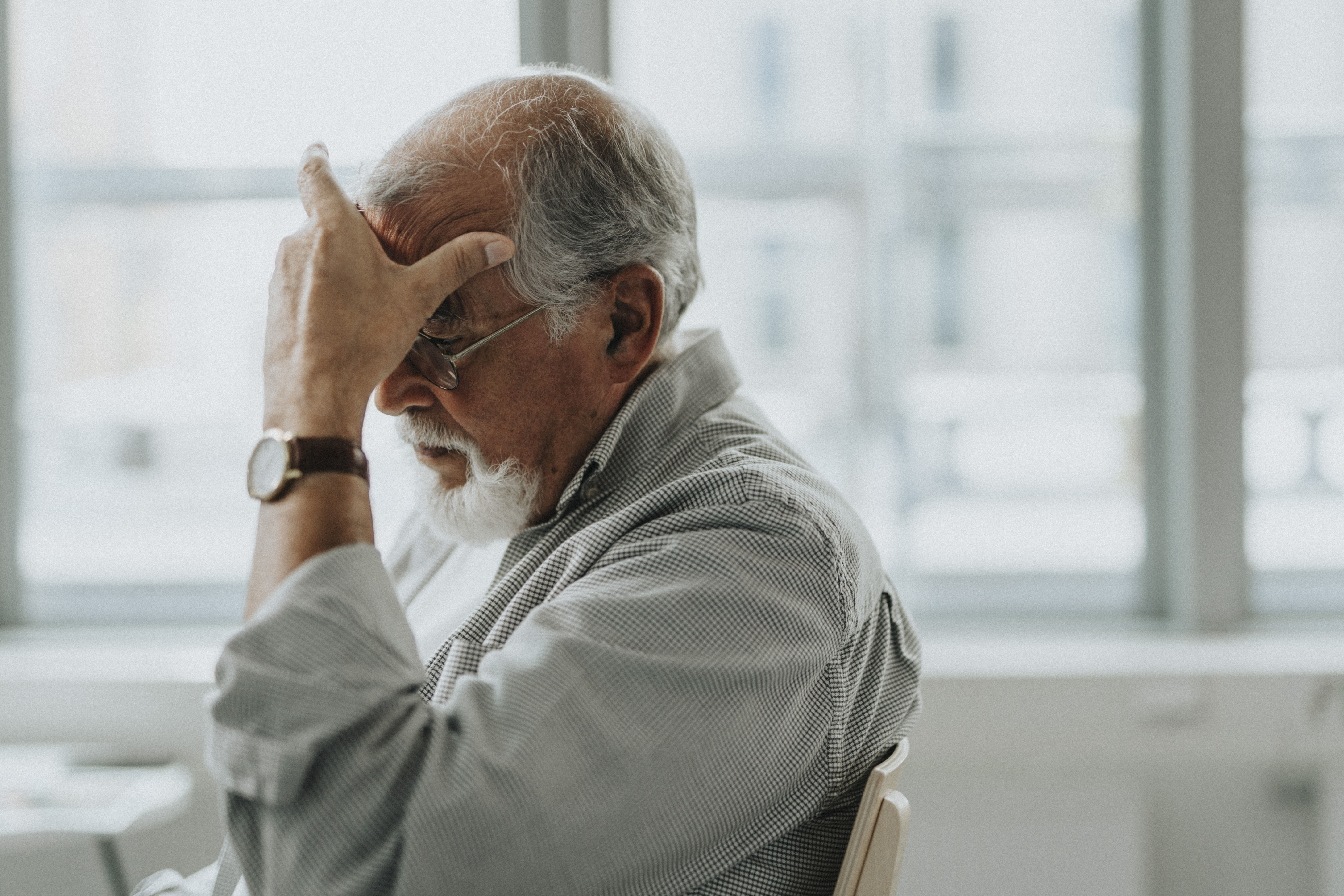 A man sitting in a chair with his hand rubbing his head.