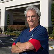 Good Samaritan RN Mark Youngblood smiles with his arms crossed, wearing eyeglasses and hospital scrubs..