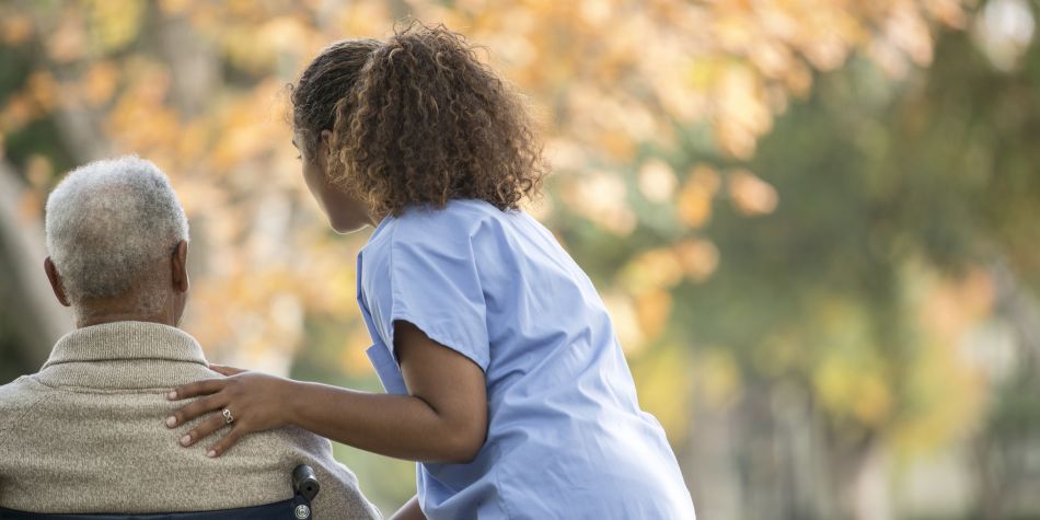 A female nurse pushing a male senior patient in a wheelchair.