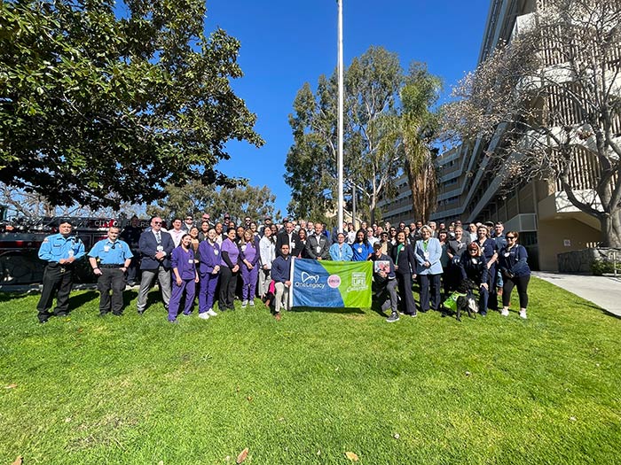 A group of hospital staff smile while standing together around the hospital flagpole, holding a Donate Life banner.