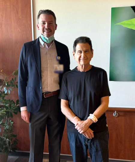 Surgeon Dr. Nels Carroll poses with his patient Dr. Michael Glazer in a hallway.