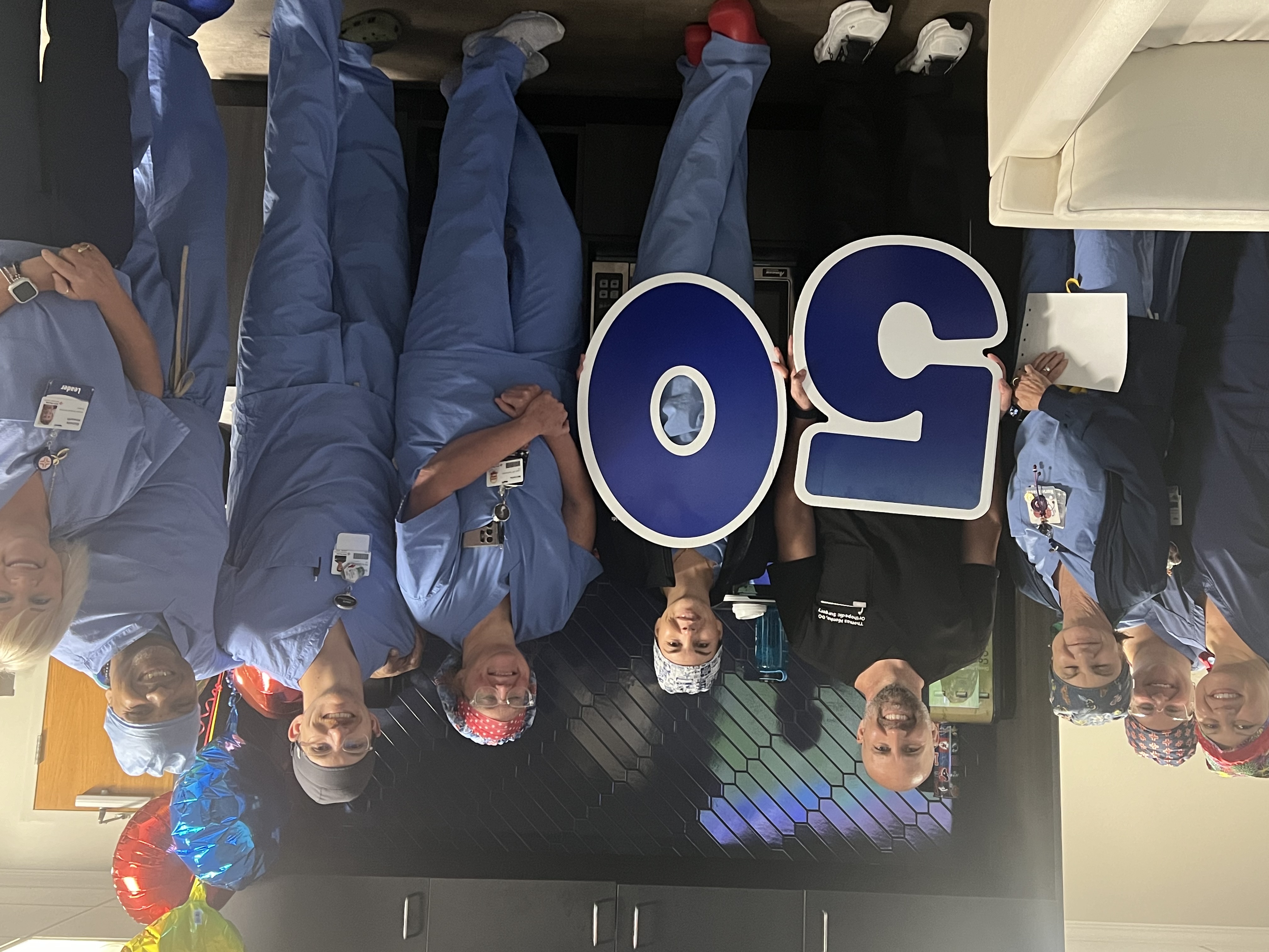 OR team celebrating 50th procedure with balloons and big "50" cut-out