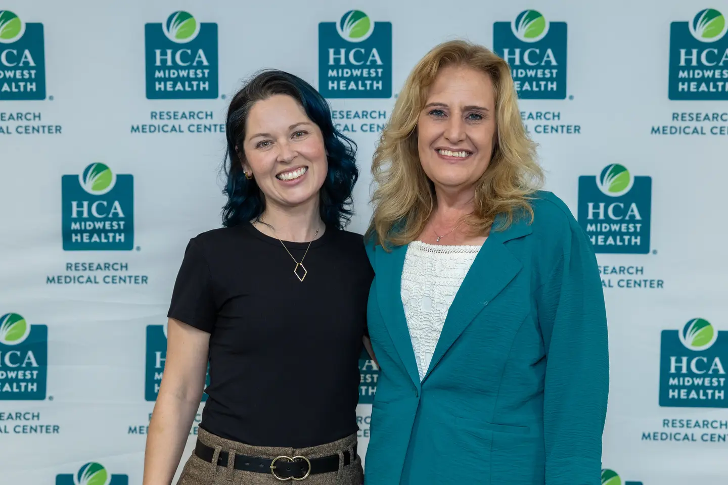 Two women smiling in front of a HCA Midwest billboard.