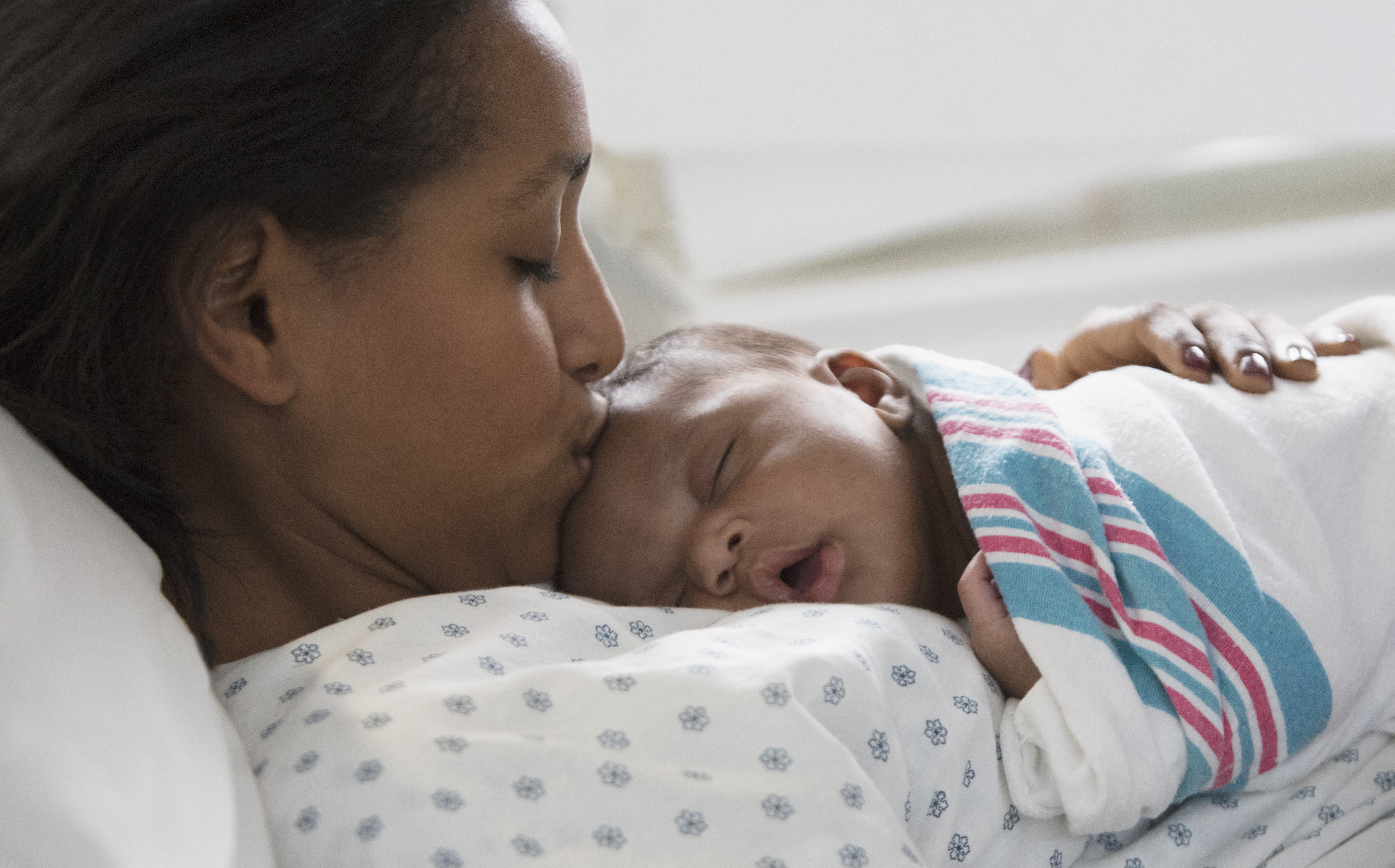 A mother in a hospital gown kissing the head of their newborn baby.