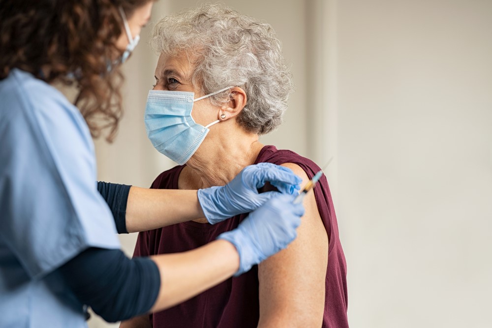 A senior woman receives a vaccine from a nurse, with both women wearing face masks.