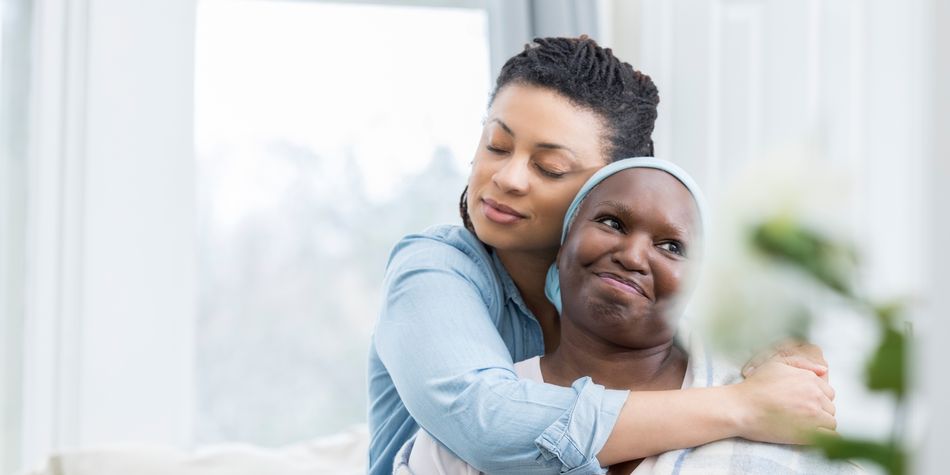A mother smiles while her daughter hugs her from behind.