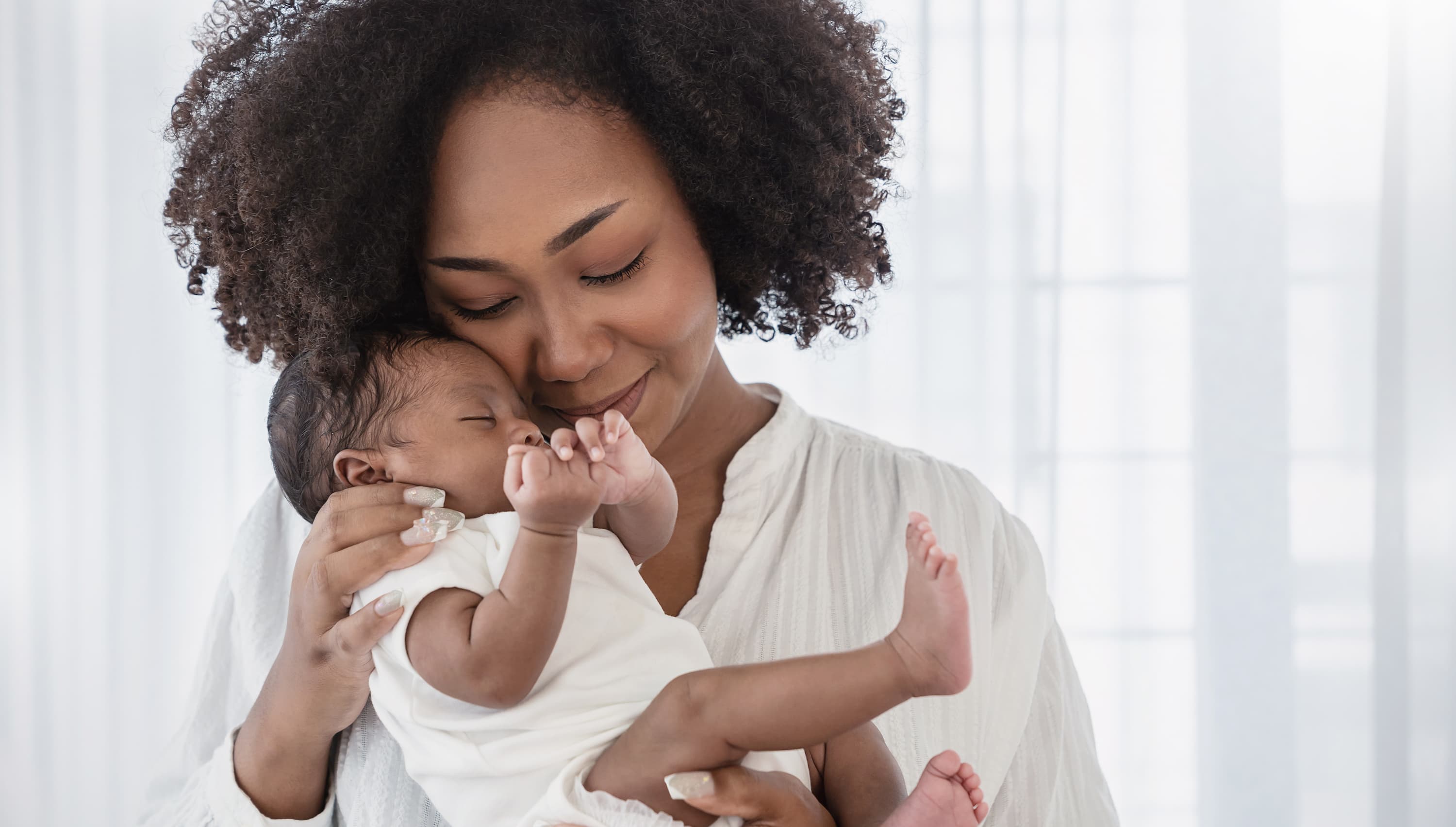 A young mother holding her newborn baby against her cheek.