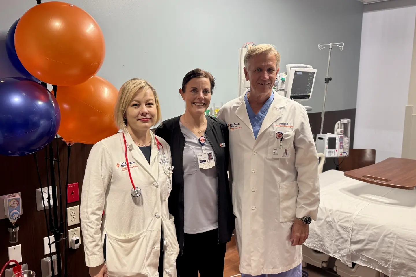 Dr. Roxana Bodin and fellow surgeon stand with a recovered Nicole Buckingham in new hospital room.