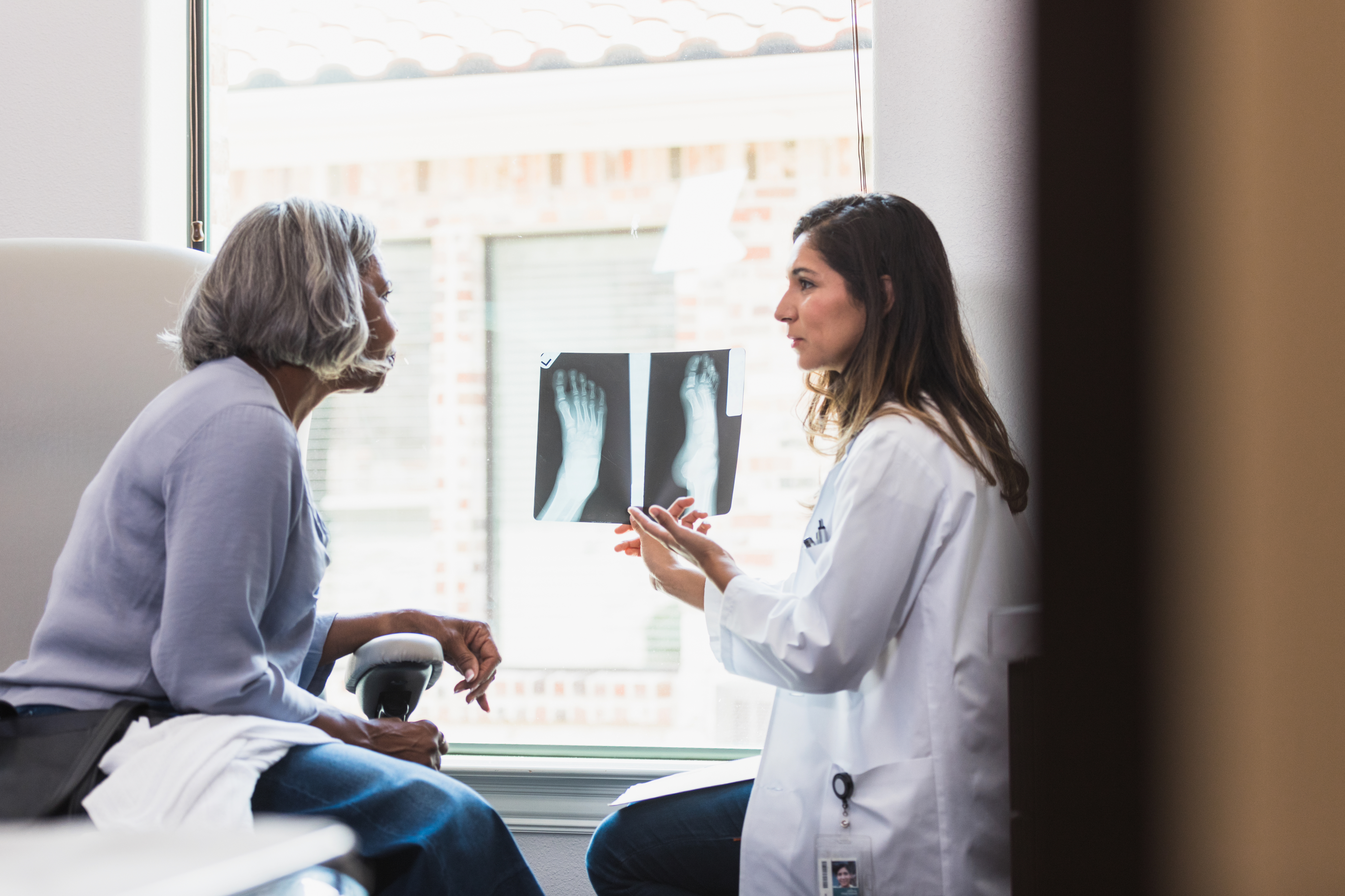 A female orthopedic doctor shows a senior female patient an x-ray of the patient's fractured foot.