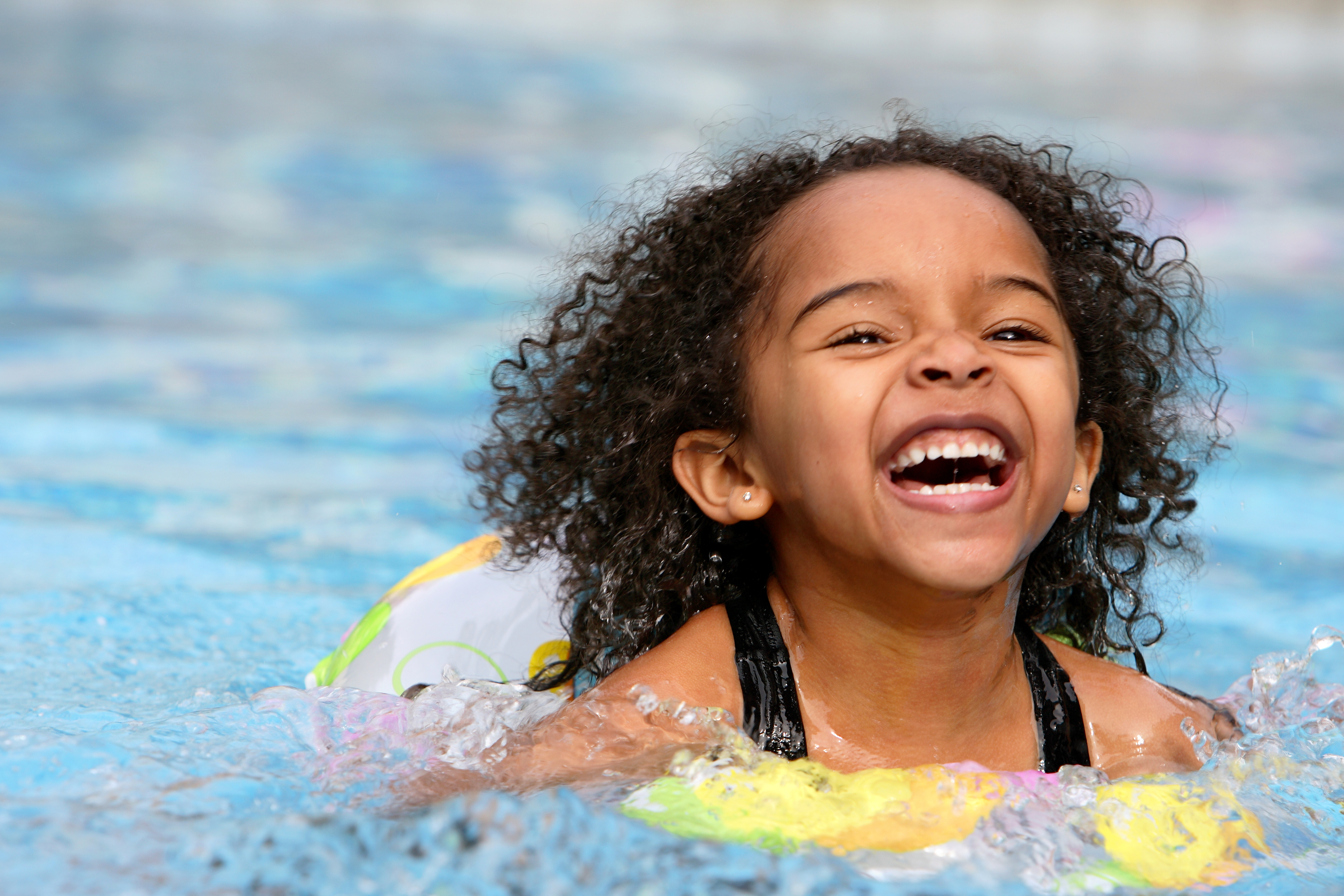 A curly toddler/child, swimming and smiling, having fun.