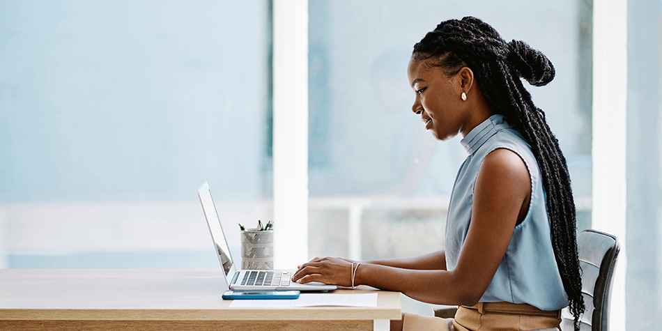 A woman sits in a conference room, working on her laptop.