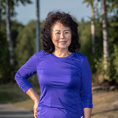 Ann smiling in a blue dress with trees in the background.