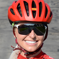 Janie smiles while wearing black cycling glasses and a red helmet