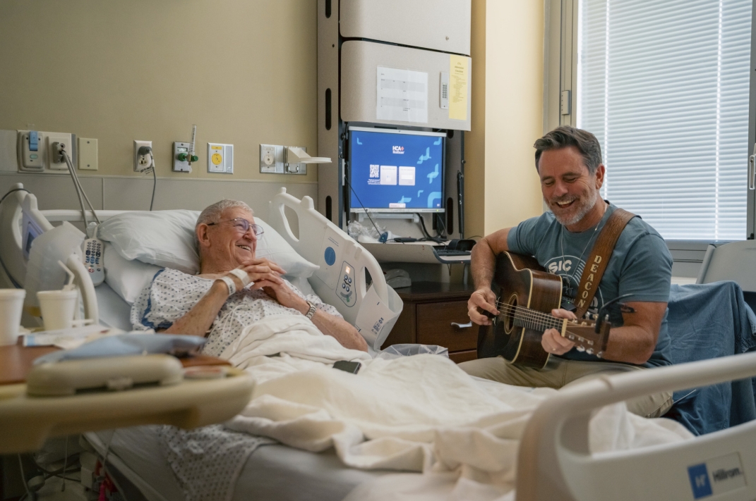 A musician playing the guitar for a patient in a hospital room