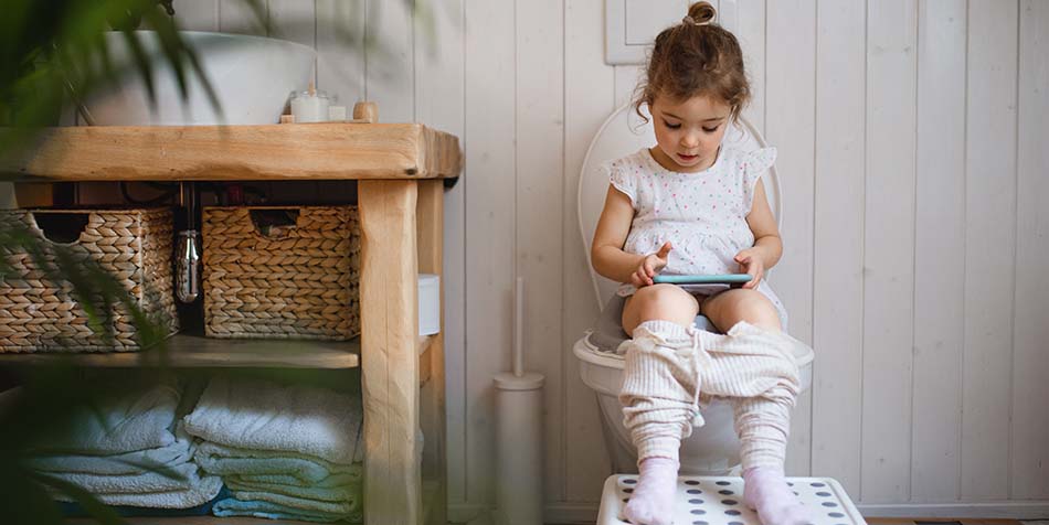 A little girl, potty training, is entertained by a mobile device.