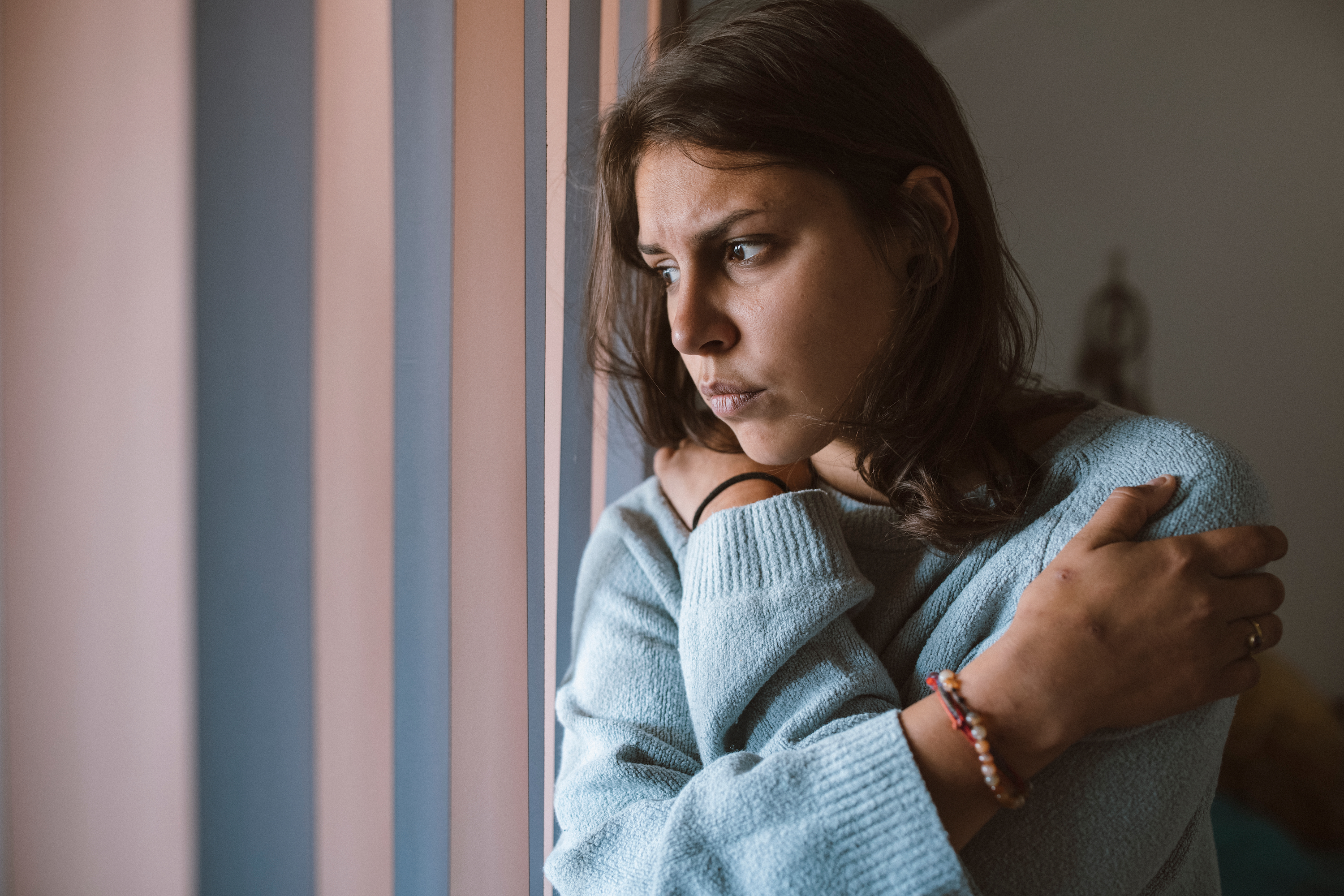 A woman looks thoughtfully out a window, appearing concerned.