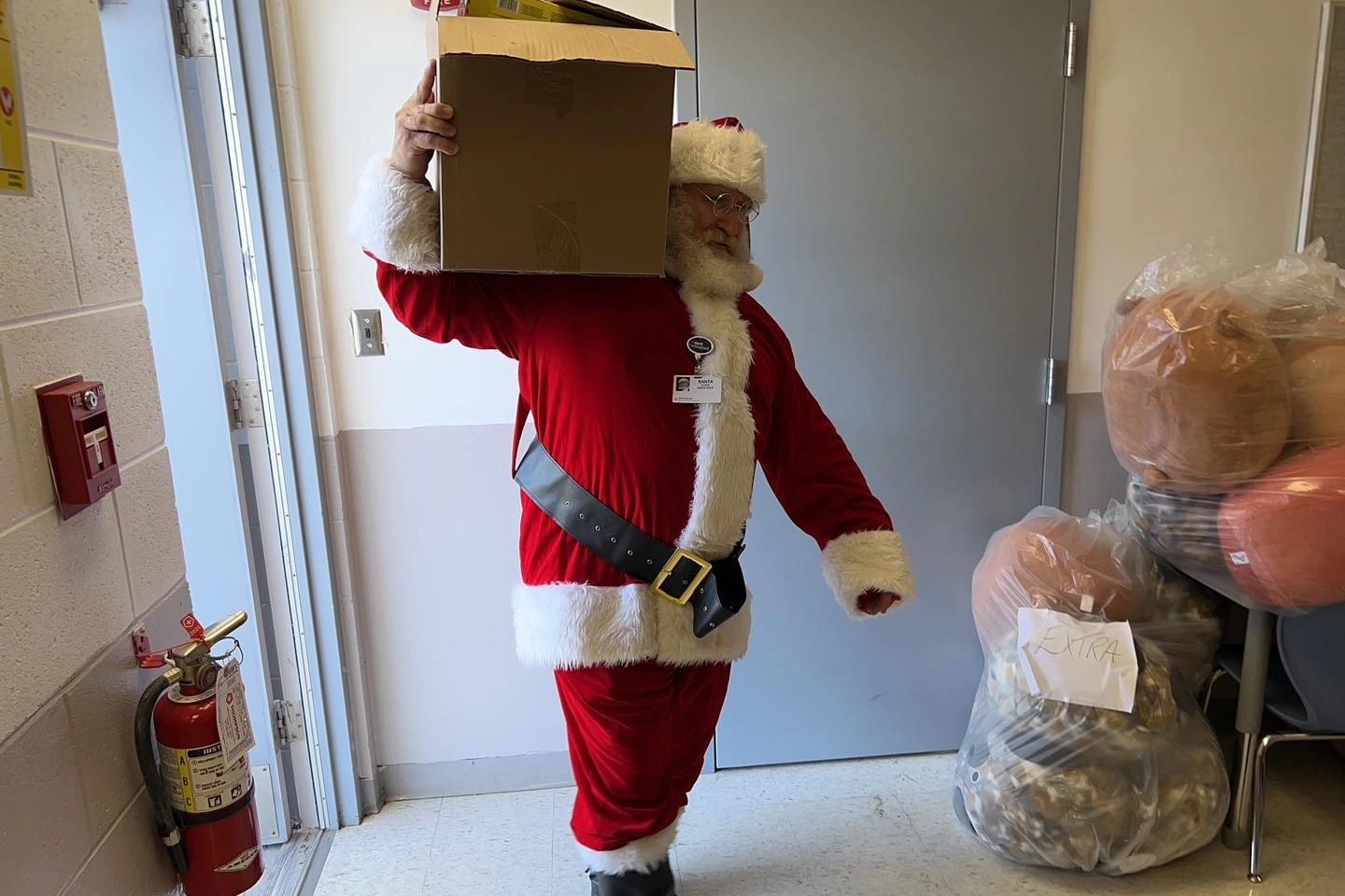 Santa is carrying a big box of toys on his shoulder into the school