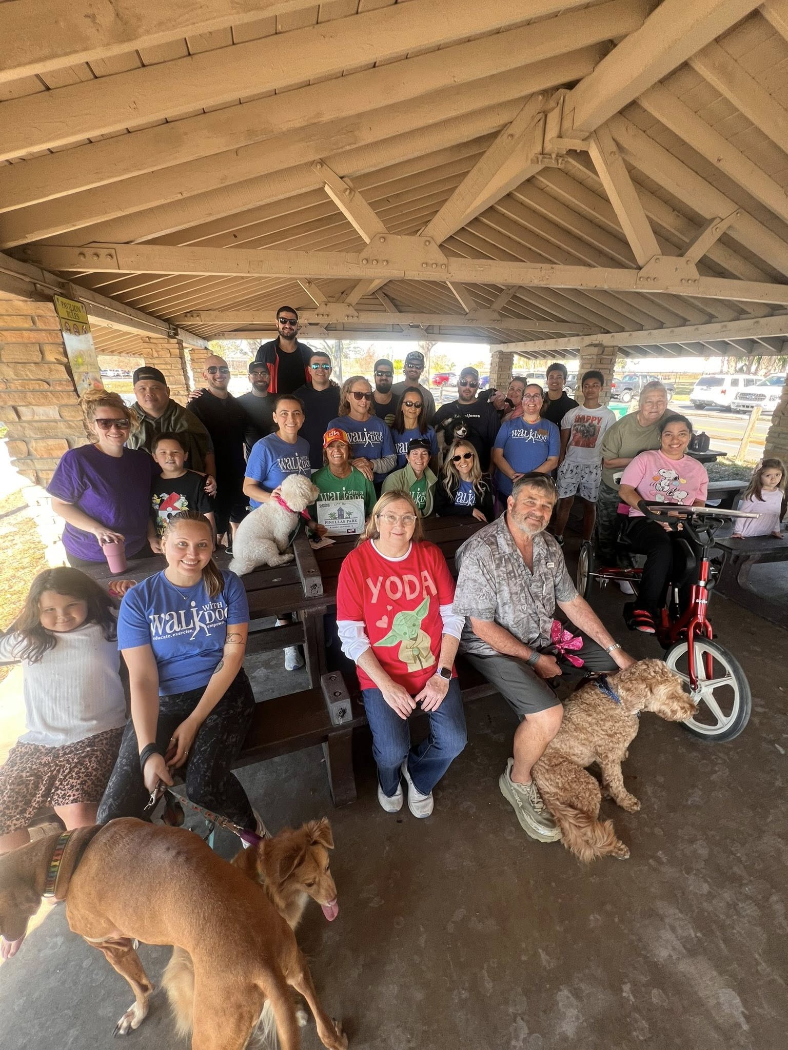 Photo showing of a group of people - some with their dogs sitting in the park, smiling for a picture.