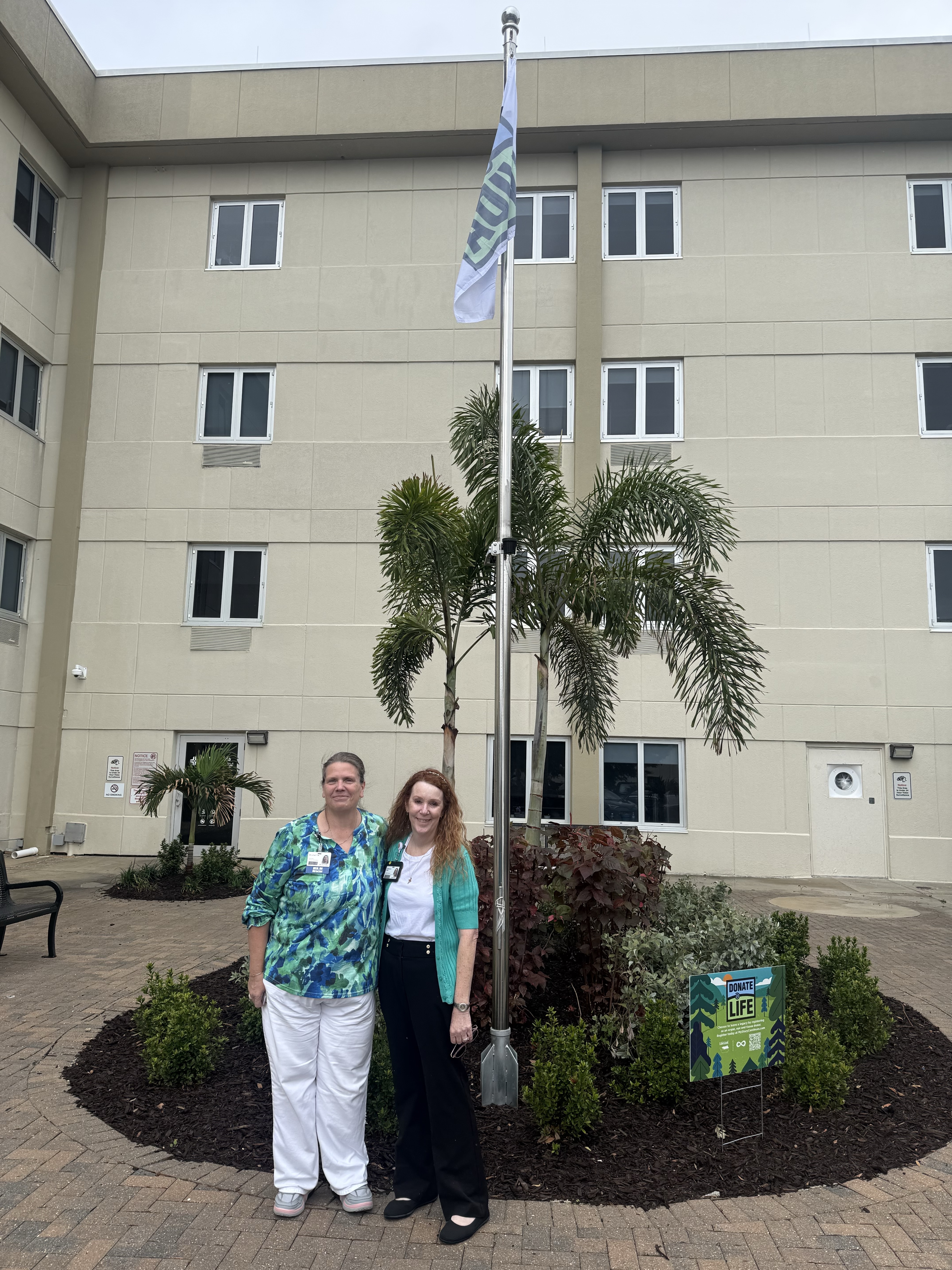 Two people standing in front of a flag pole flying a Donate Life event flag.