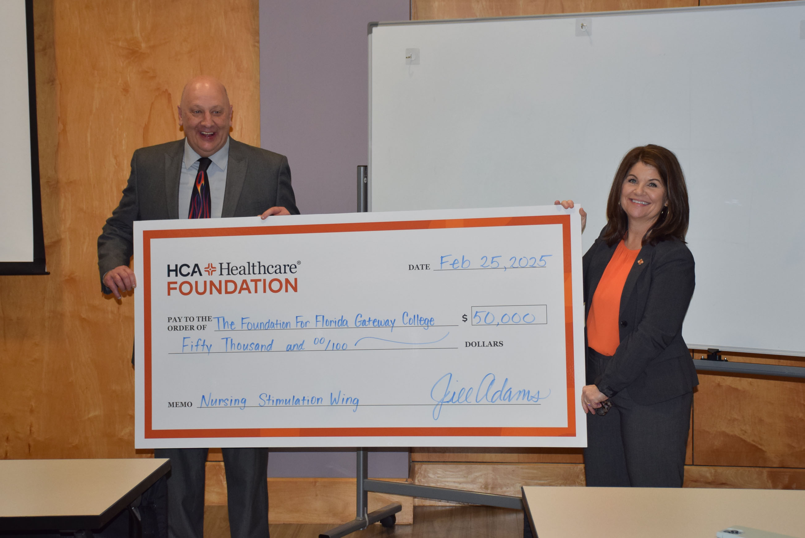 Two people standing in a room holding a large check in-between them and smiling