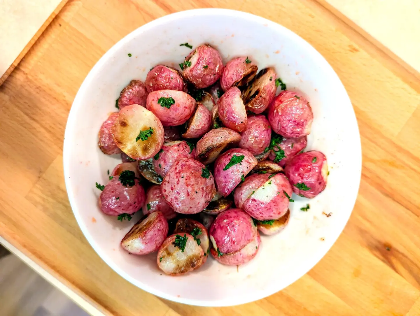 a white bowl of roasted red radishes on a wooden table