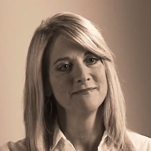 Teri smiles while wearing a collared blouse and hoop earrings.