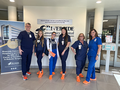 A group of female and male medical staffers dressed in hospital scrubs smiling. 