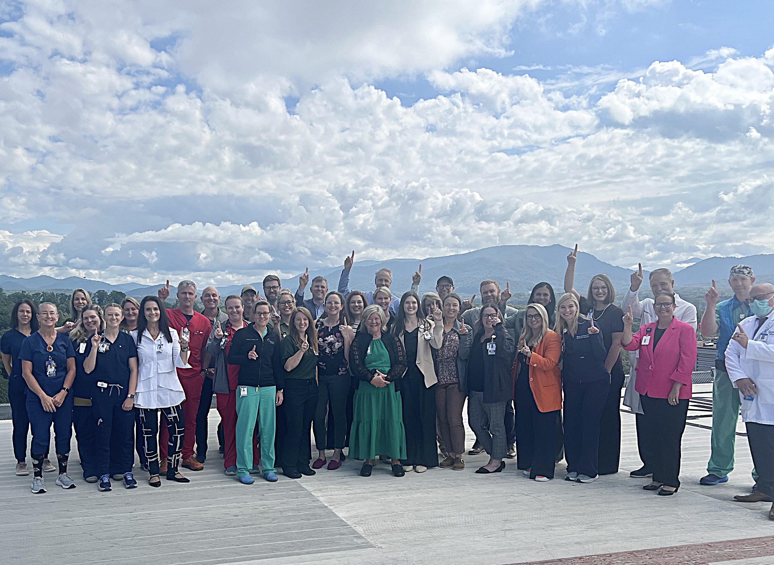 Mission Hospital trauama team outdoors, with mountain range in the background, many holding up one finger to celebrate Level 1 trauma verification.