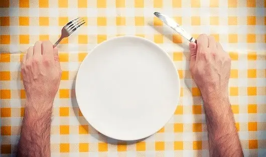 hands holding a knife and a fork on either side of an empty plate
