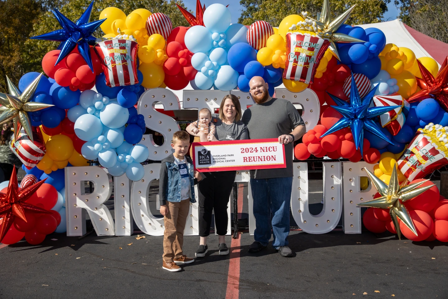 NICU family Morgan and Derek Ogan and their two NICU graduate sons, Finn and Remi, posing under blue, red, yellow, silver, and white balloons