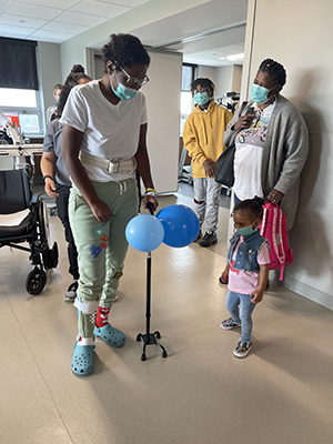 Ramoni smiles while using a cane to walk during recovery from being shot.