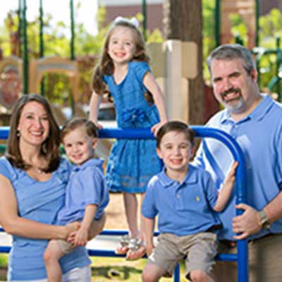Craig smiles while standing next to a playground with his wife and three kids.