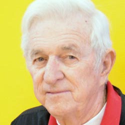 Billy Allgood smiles while wearing a white tshirt and a black and red jacket.
