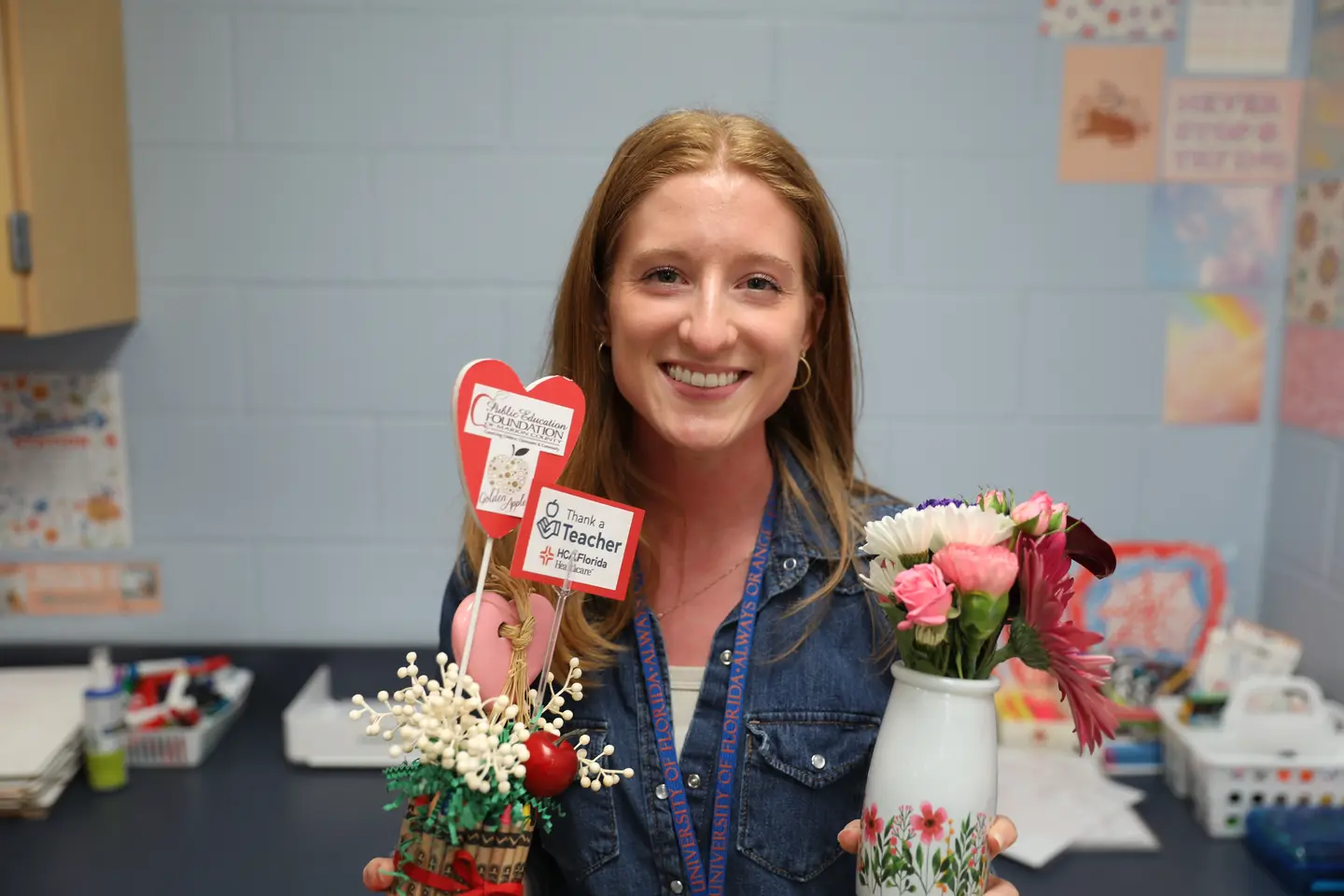 Claire Sensibaugh holding two vases with flowers and Thank a Teacher signage.