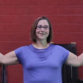 Melissa smiles for the camera, while flexing her biceps in a gym.