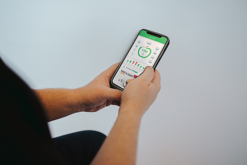 A person holds a phone up, showing an app that helps keep track of calories and nutrition goals.