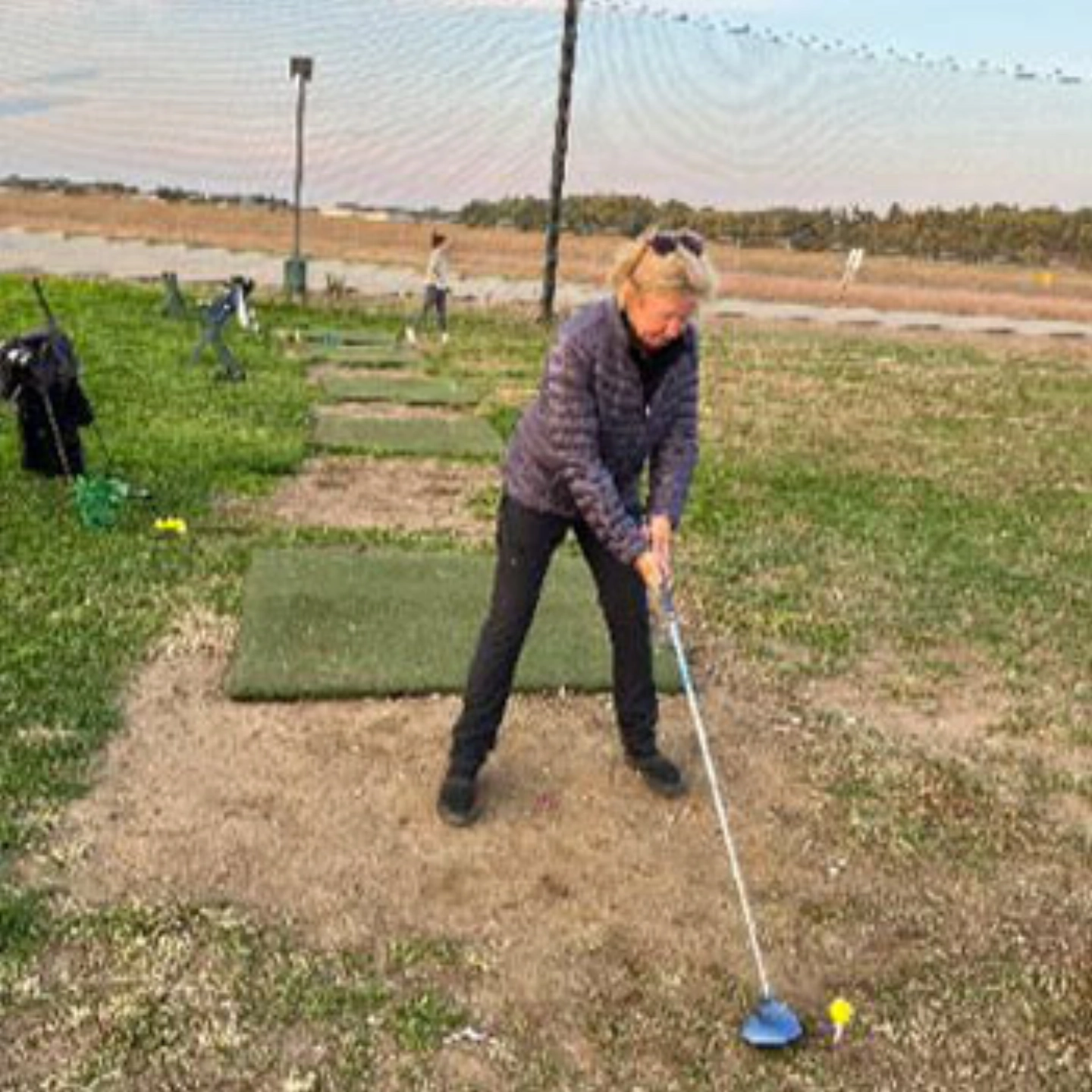 Carolyn about to swing at her golf ball, at a driving range outdoors.