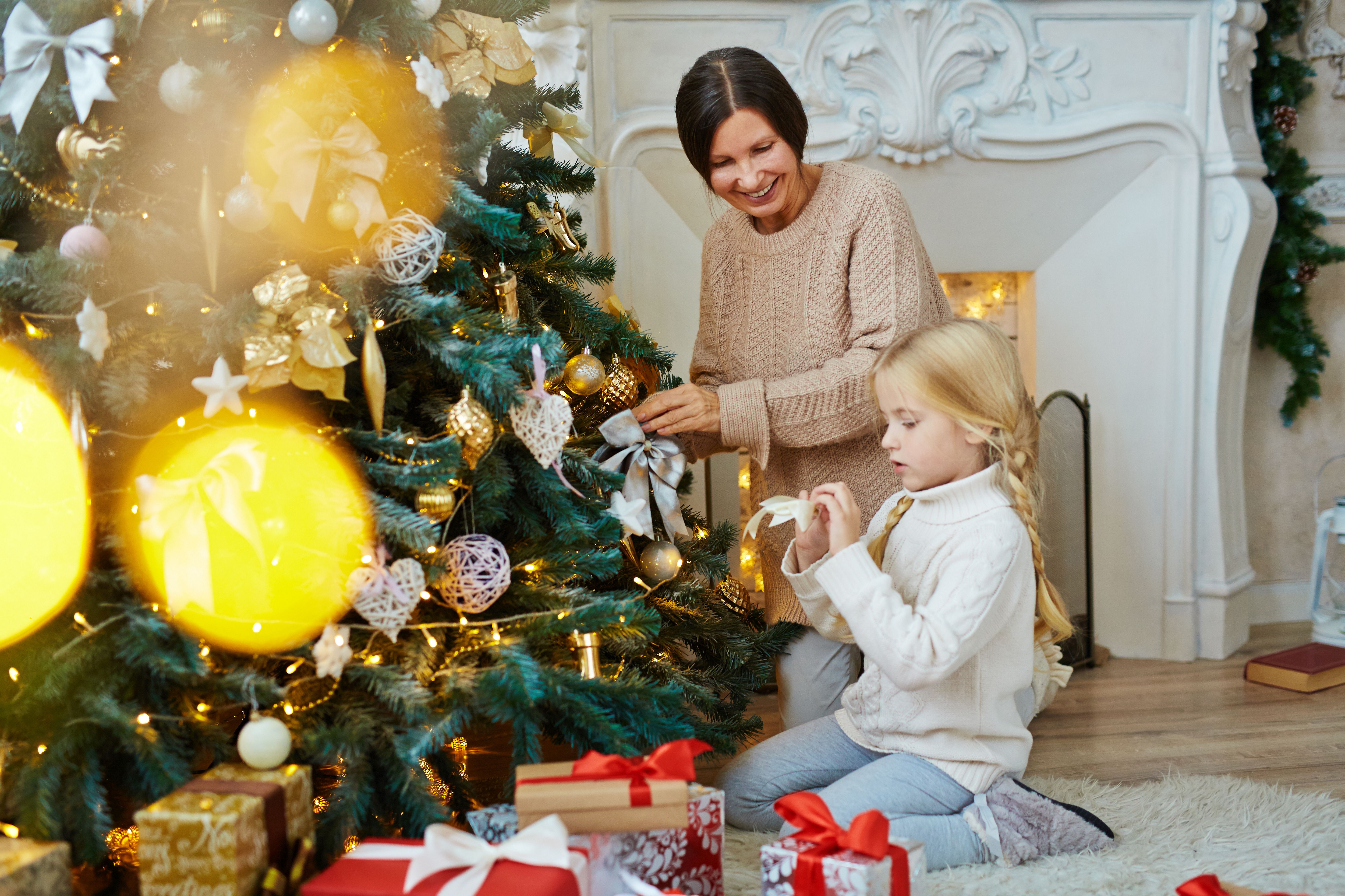 A smiling woman and young girl hang ornaments on a Christmas tree