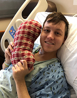 Mason Bettes in his hospital bed smiling with a kidney pillow.