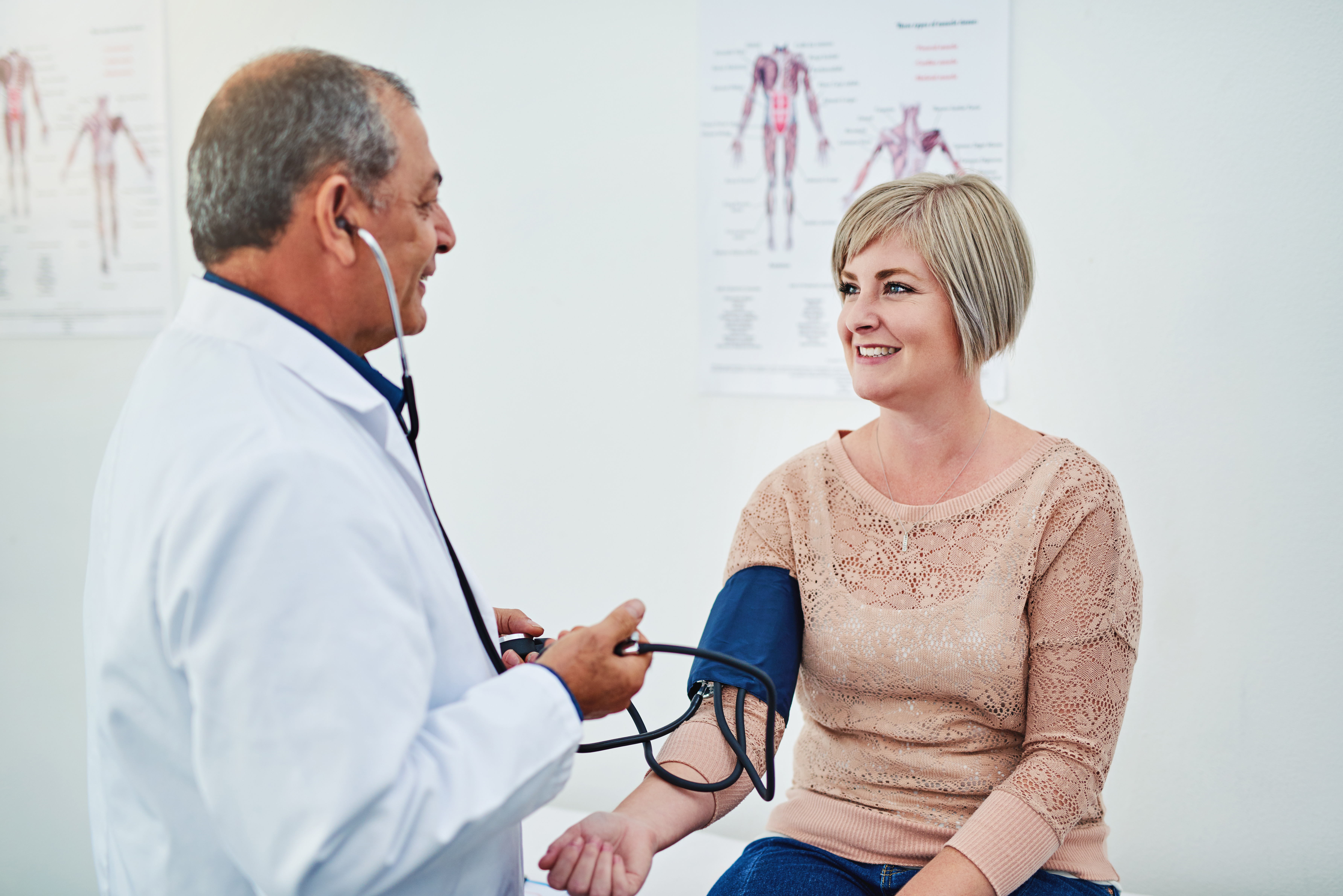 A doctor is checking a patients blood pressure while she is seated in an exam room.