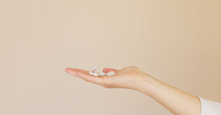 A person holds several white vitamin pills in the palm of their hand.